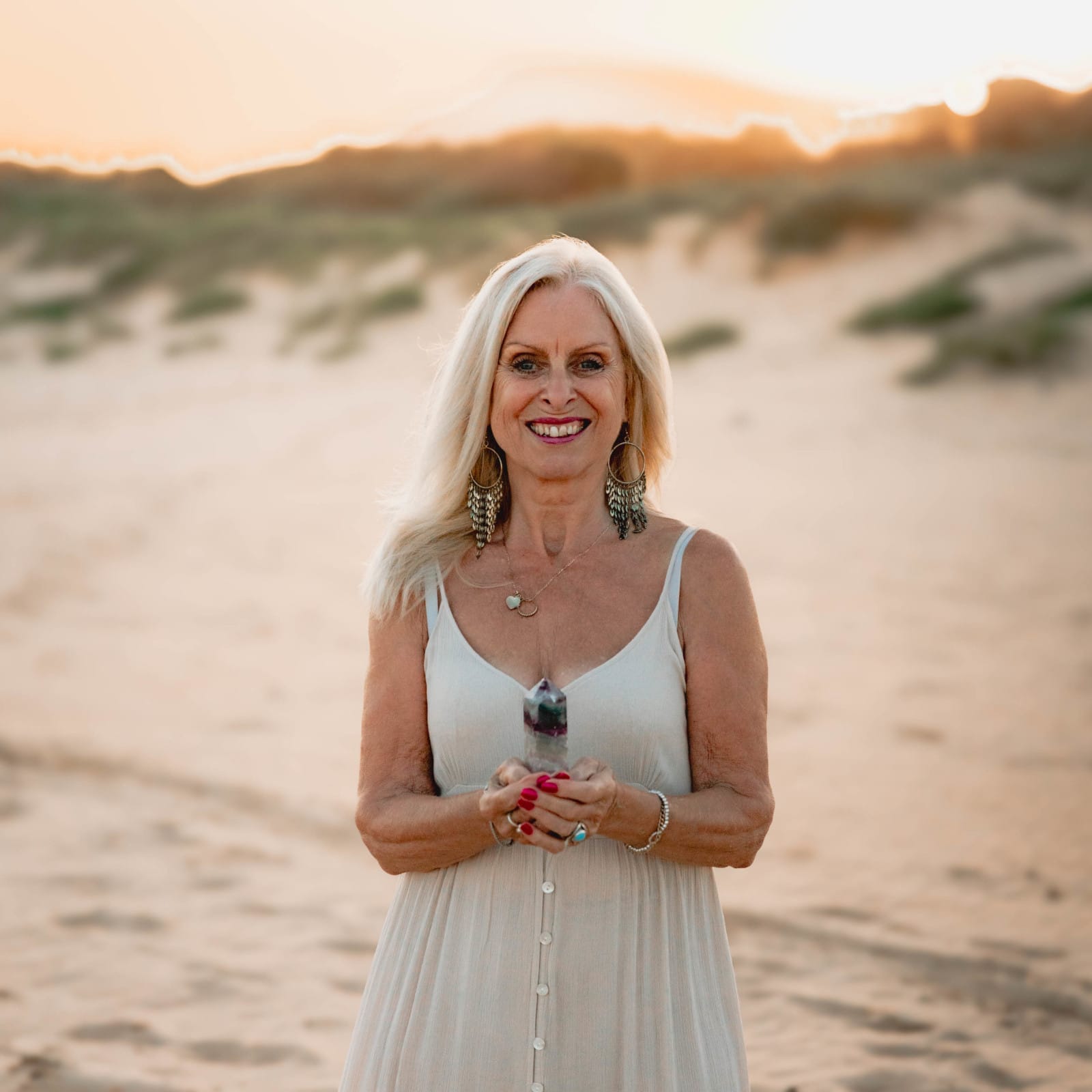 Val Hood, an Evidential Medium, stands on the beach, holding a stunning crystal, radiating peace and tranquility.