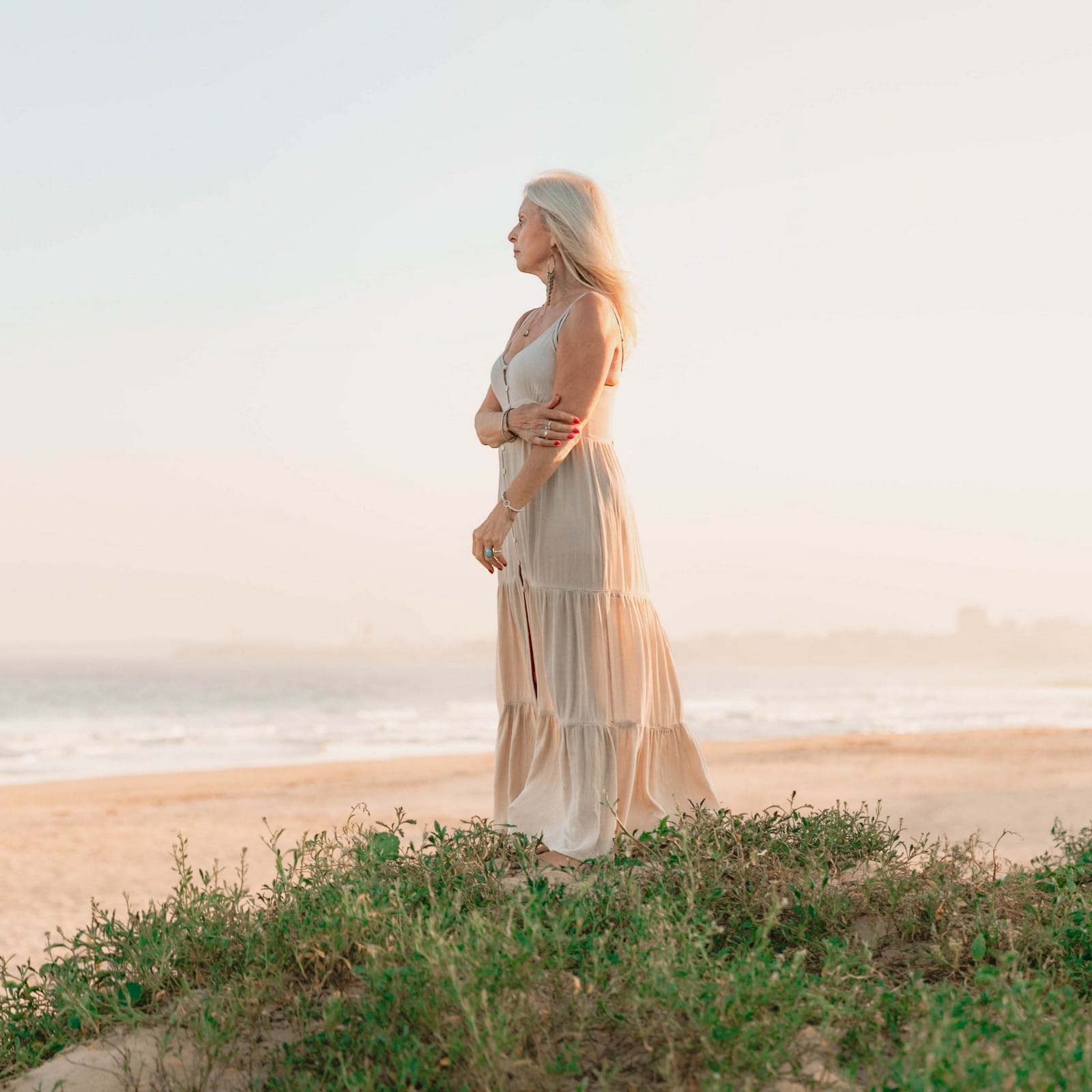 Val Hood, an Evidential Medium, stands on the beach in a flowing dress, radiating calm and spiritual energy.